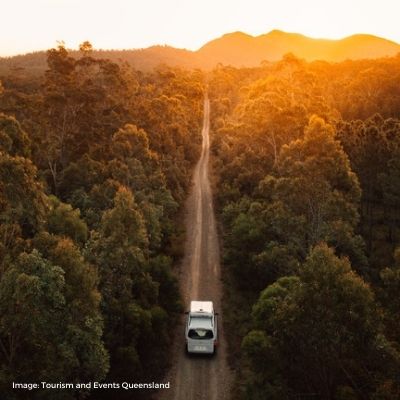 Tourism and Events Queensland - aerial shot of car driving through forest road at sunset