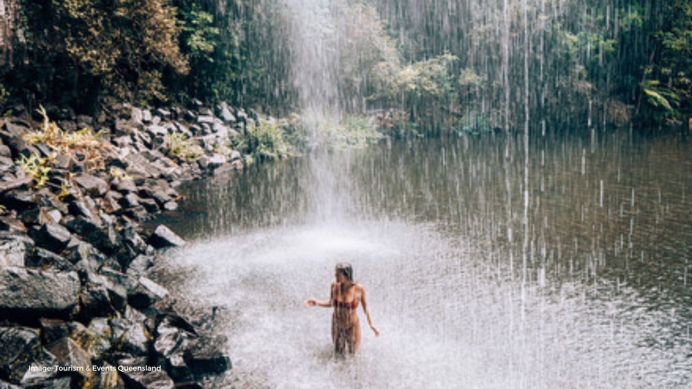 Girl standing underneath Millaa Millaa Waterfall | Tourism and Events Queensland