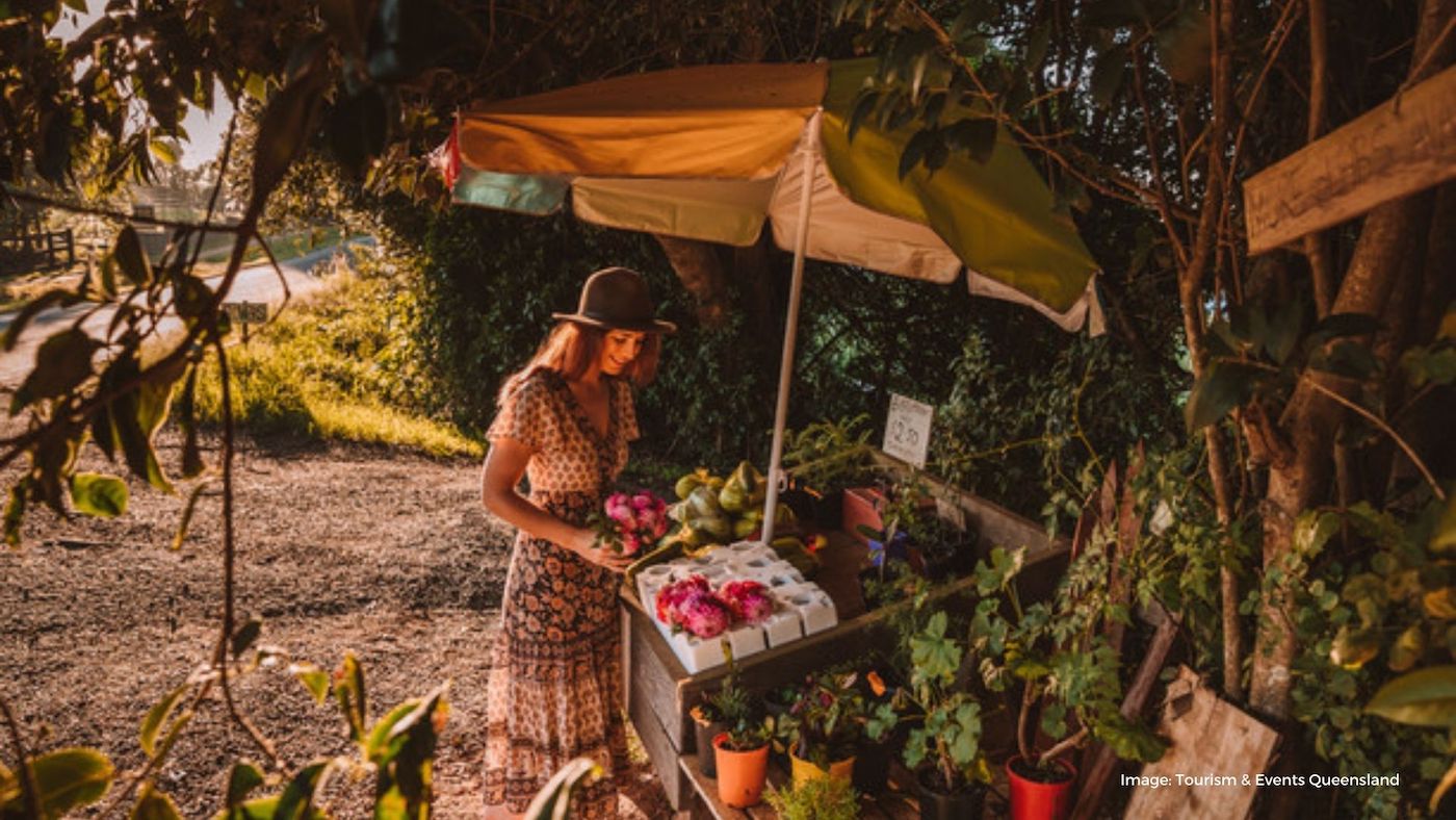 Woman standing at fruit market stall | Tourism and Events Queensland