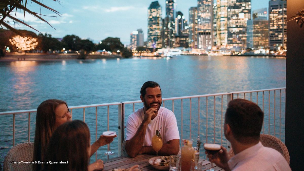 Group sitting and enjoying drinks next to Brisbane river with skyline in background | Tourism & Events Queensland