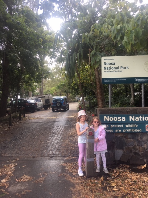 Two young girls stand in front of the Noosa National Park sign