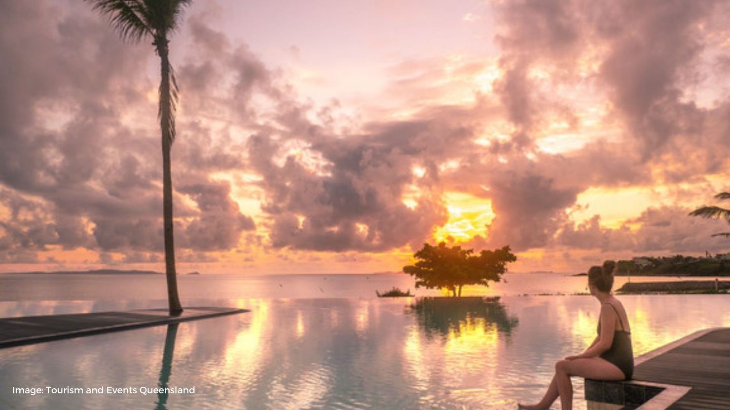 Woman sitting at infinity style pool lagoon at sunrise | Tourism and Events Queensland