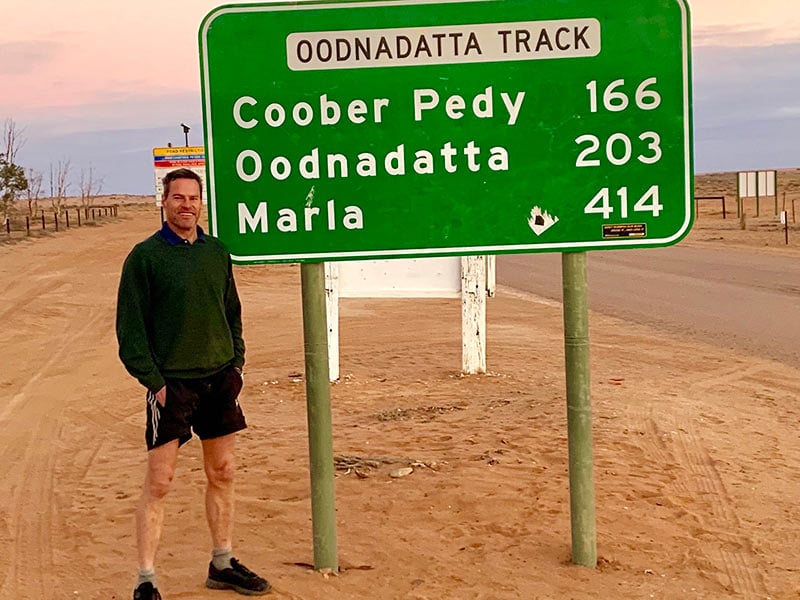 Andrew standing in front of the Oonadatta Track road sign