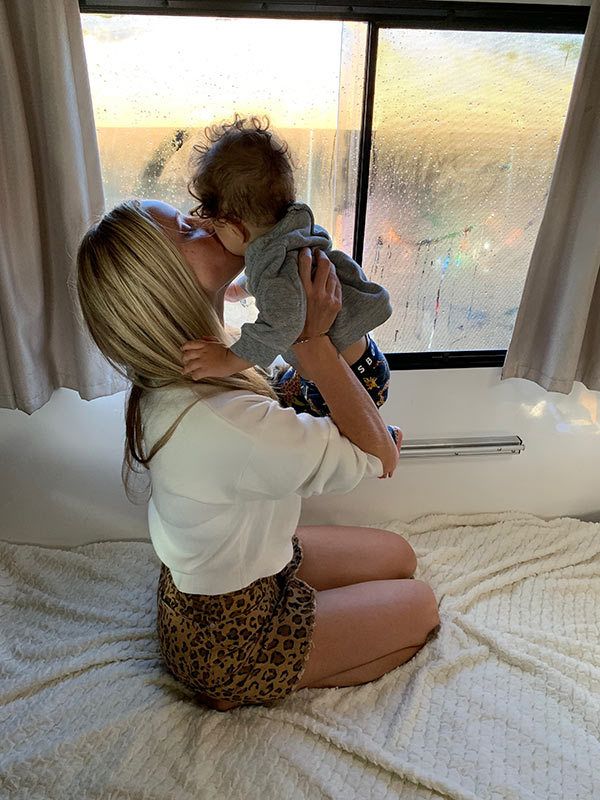 Steph Luck holding and kissing her son inside an Apollo Motorhome in the morning light
