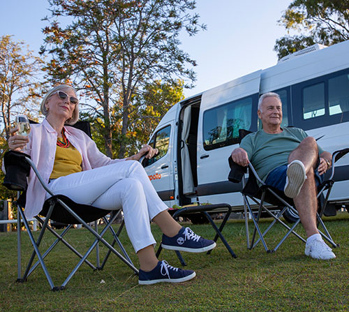 Senior couple sit in camp chairs by their Apollo campervan